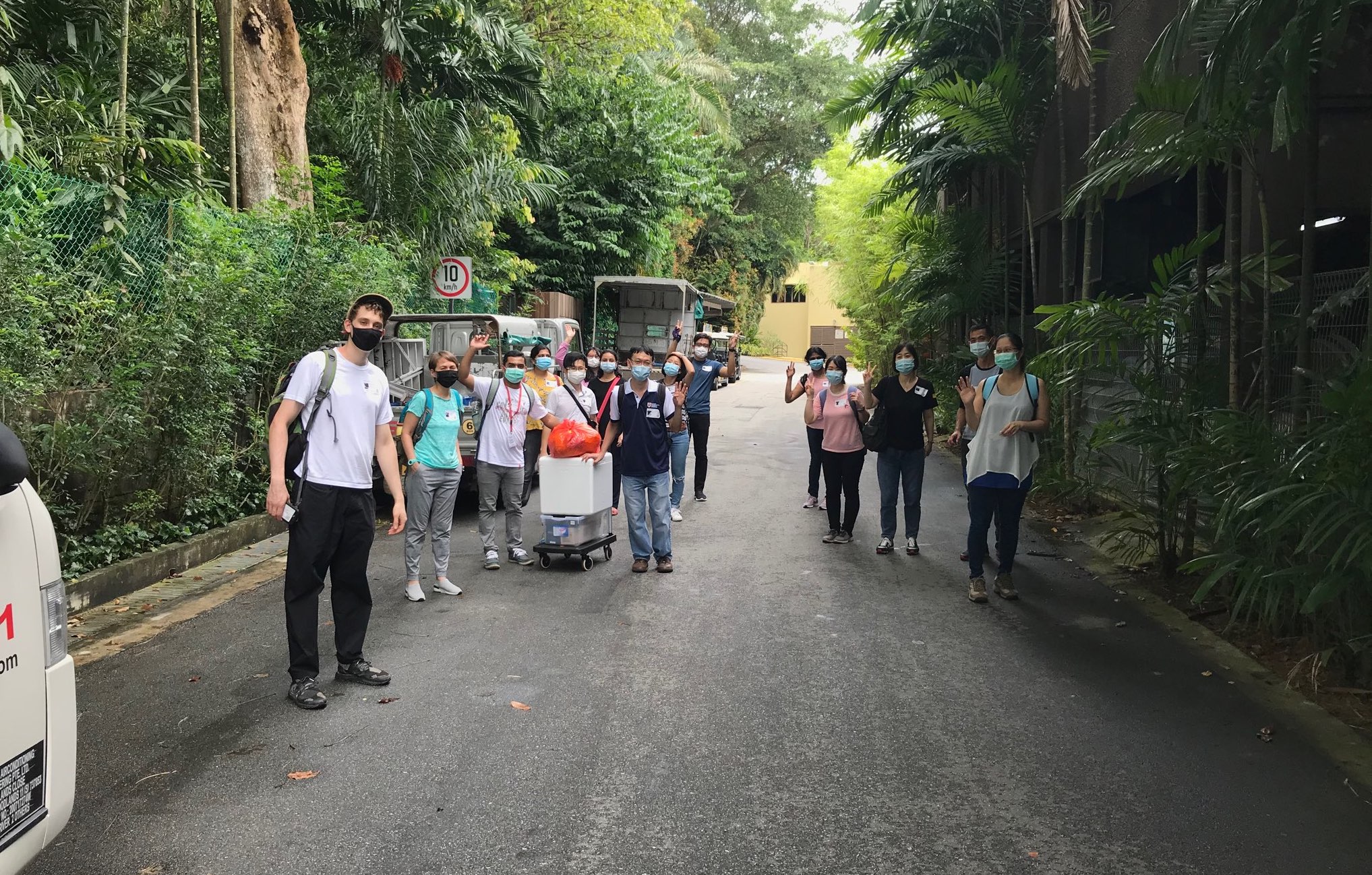 SCELSE air microbiome team gathers on a forested road at an outdoor sampling site with sampling equipment on trolly's. Team members each wear face masks for covering during COVID-19 Singapore re-opening