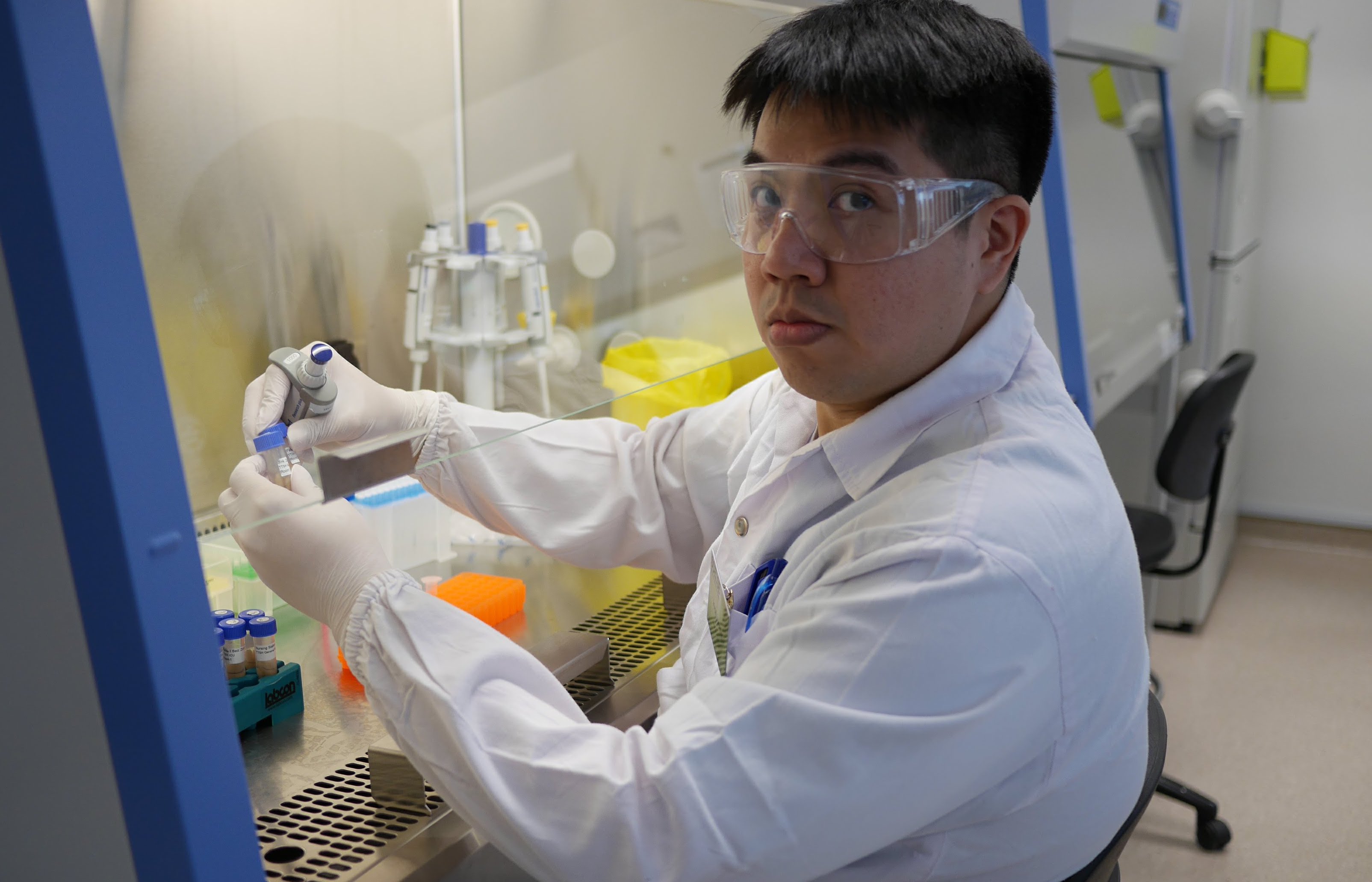 SCELSE researcher Dr. Irvan Luhung performs lab work at a biosafety cabinet in a lab coat and goggles