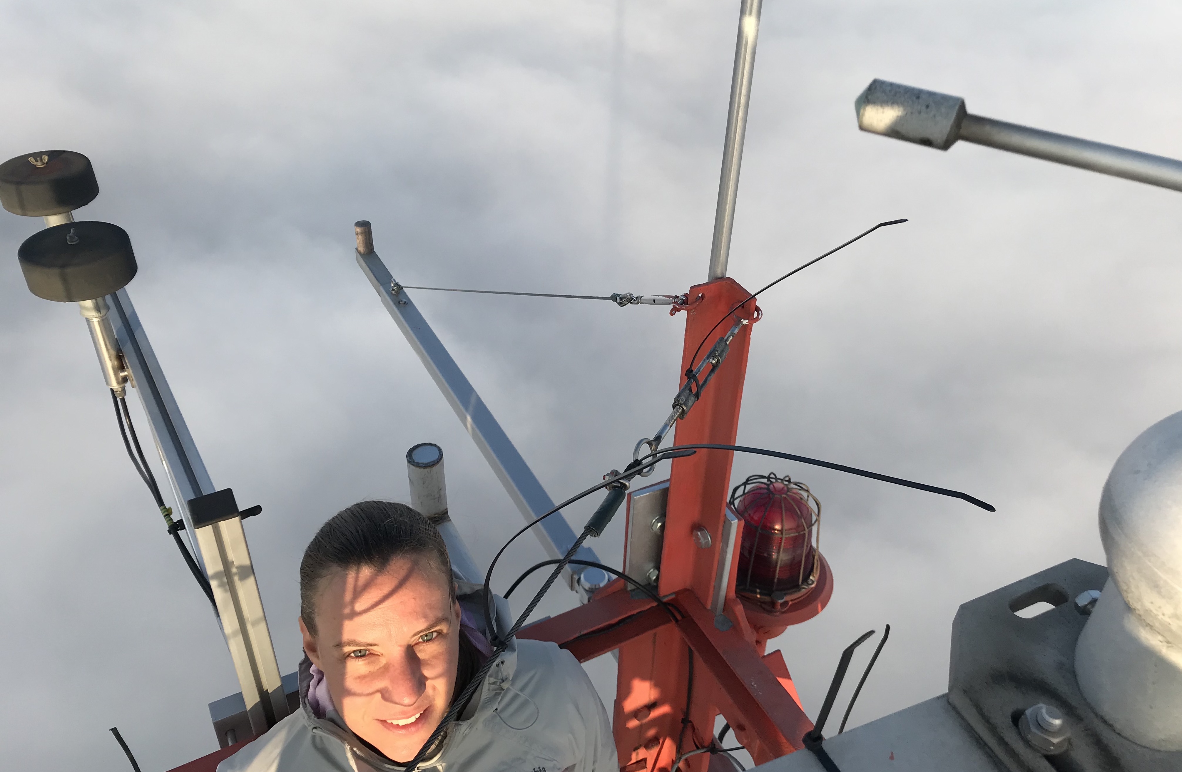 Dr. Daniela Moses above a layer of blue grey clouds at the top of the KIT meteorological tower